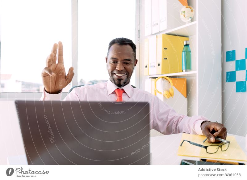 Glücklicher schwarzer Geschäftsmann führt Videogespräch auf Laptop im Büro Gruß Videoanruf Lächeln maskulin professionell unabhängig benutzend Apparatur Mann