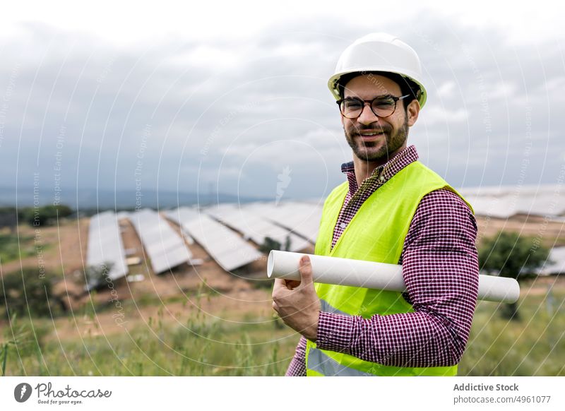 Positiv gestimmter Mann mit Bauplan in der Nähe eines Solarparks Ingenieur solar Kraft Station Tiefgang Lächeln positiv Arbeit Landschaft männlich professionell