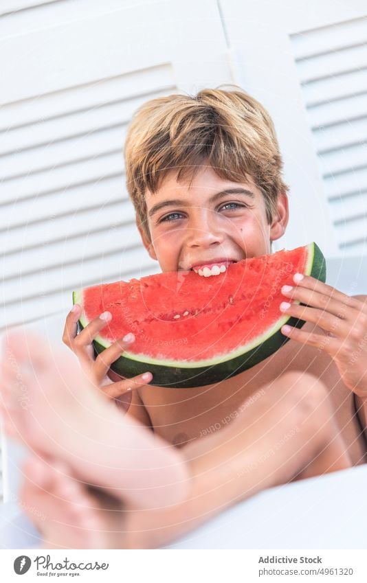Fröhlicher Junge isst saftige Wassermelone im Sommer essen genießen Saft reif frisch Glück Teenager Scheibe Stuhl sitzen Frucht geschmackvoll zufrieden Lächeln