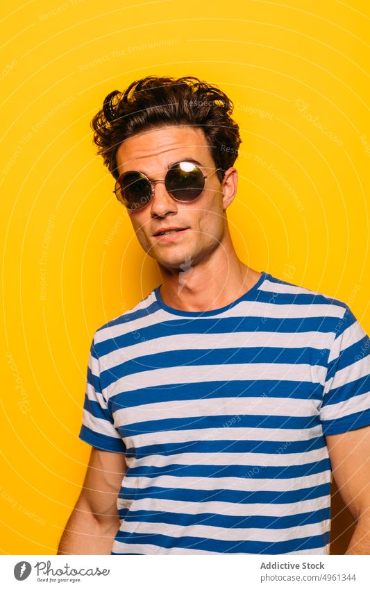 Stilvolles Modell mit modernem Haarschnitt auf gelbem Hintergrund in die Kamera schauen Mann Sonnenbrille trendy auflehnen Streifen farbenfroh Porträt