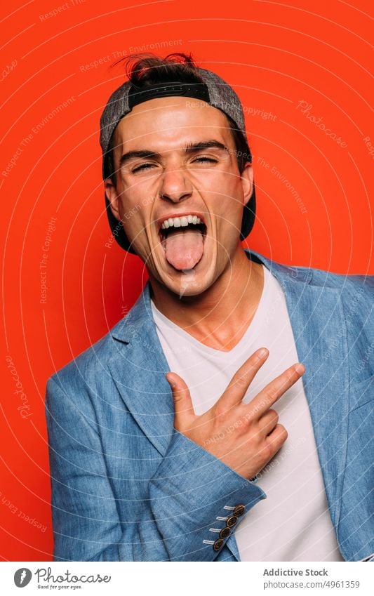 Stilvoller Mann mit herausgestreckter Zunge auf rotem Hintergrund ausspannen Rap Mode cool Individualität Gesicht machen unverschämt stylisch Porträt modern