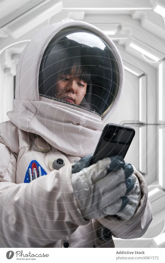 Astronautin benutzt Smartphone im Raumschiff Frau benutzend Raumanzug futuristisch Gang Wissenschaft Missionsstation jung asiatisch Chinesisch Japanisch