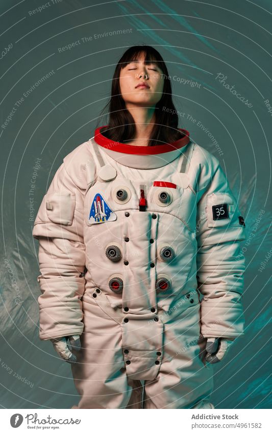 Ruhiger asiatischer Kosmonaut mit geschlossenen Augen im Studio Frau bereit Missionsstation Windstille ernst geschlossene Augen Raumanzug futuristisch modern