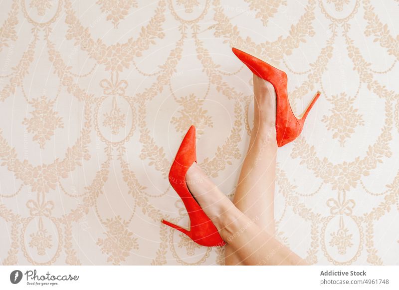 Frau in Schuhen kreuzt Beine an der Wand Beine gekreuzt Stiletto Ornament Tapete elegant hell rot Damenschuhe feminin lebhaft pulsierend tagsüber stilvoll