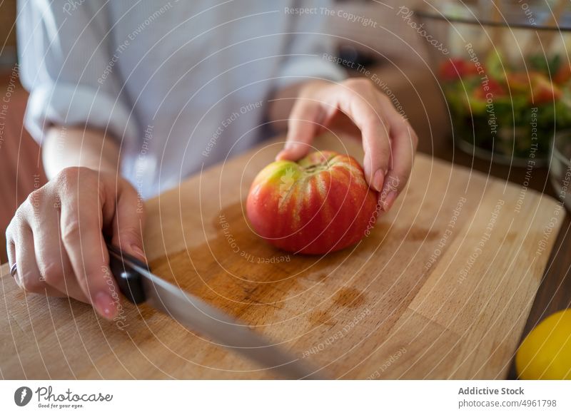 Crop-Frau schneidet Tomate für Salat geschnitten Schneidebrett Koch Salatbeilage frisch heimwärts Küche Mittagessen Messer vorbereiten Scheibe Gemüse