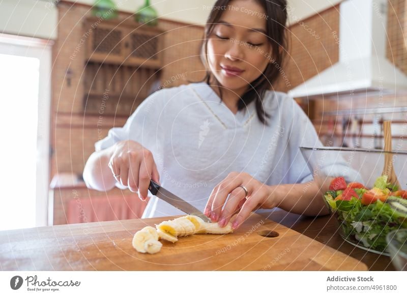 Asiatische Frau schneidet Banane in der Küche geschnitten Koch Salatbeilage heimwärts gesunde Ernährung Diät Schneidebrett asiatisch ethnisch Frucht organisch
