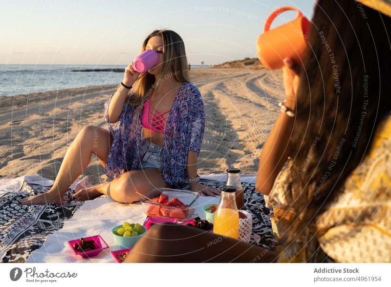 Unterschiedliche Freundinnen trinken am Strand Frauen MEER Sonnenuntergang Picknick Zusammensein Wochenende Sommer Decke schlürfen Feiertag multiethnisch