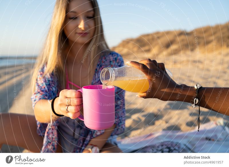 Anonyme schwarze Frau gießt Saft für Freundin Frauen eingießen Picknick Strand Sommer Zusammensein Wochenende trinken vielfältig rassenübergreifend