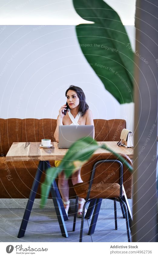 Geschäftsfrau, die während der Arbeit mit ihrem Smartphone spricht und auf ihrem Laptop surft reden Projekt Café Browsen multitask Unternehmer Frau abgelegen