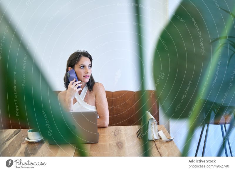 Geschäftsfrau, die während der Arbeit mit ihrem Smartphone spricht und auf ihrem Laptop surft reden Projekt Café Browsen multitask Unternehmer Frau abgelegen