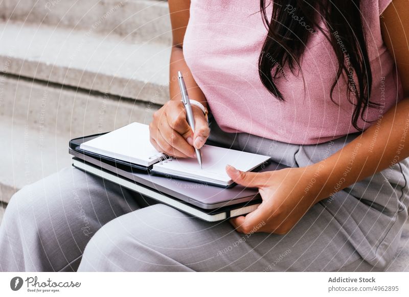 Unbekannte Frau, die auf einer Treppe auf der Straße sitzend Notizen in ein Notizbuch schreibt zur Kenntnis nehmen Notebook freiberuflich schreiben Laptop
