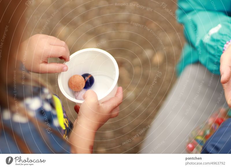 Ein Kind spielt mit Murmeln in einem Becher. Eine erwachsene Person kniet daneben. Kinderspiel spielen kindheit gemeinsames spiel Spaß Kinderhände