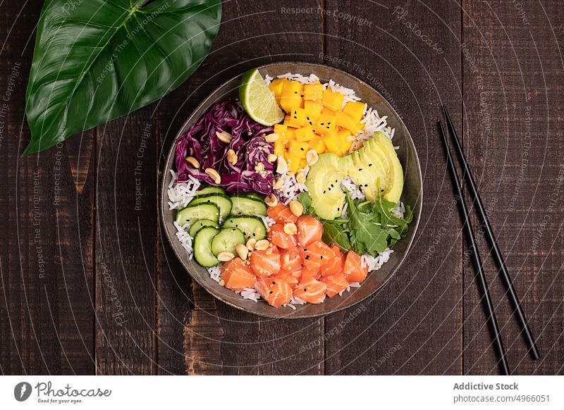 Leckere Poke-Bowl mit verschiedenen Gemüsesorten, Reis und Lachs stoßen Avocado Mango Asiatische Küche Essstäbchen gesunde Ernährung Salatgurke Speise Fisch