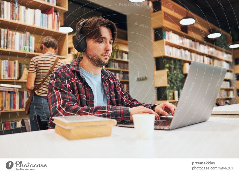 Student lernt in der Universitätsbibliothek. Junger Mann bereitet sich am Laptop auf einen Test vor. Mann hört sich einen Online-Kurs an. Konzentrierter Student, der für College-Prüfungen lernt