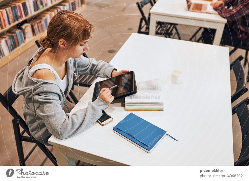 Studentin lernt in der Universitätsbibliothek. Junge Frau schreibt Aufsatz und macht Notizen mit Computer-Tablet. Konzentrierter Student, der für College-Prüfungen lernt