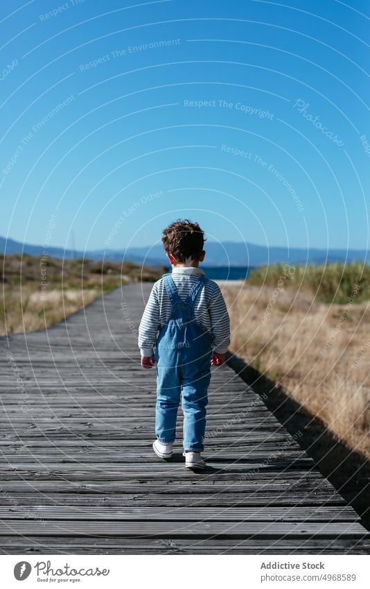 Kleiner Junge auf der Uferpromenade im Feld Promenade Landschaft allein Sommer Blauer Himmel sorgenfrei Laufsteg schlendern Weg Kind Spaziergang ländlich