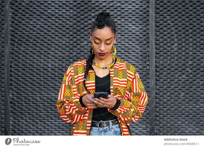 Stylische Frau benutzt Smartphone auf der Straße Stil Wand urban jung benutzend ethnisch modern Browsen trendy Streetstyle online Internet farbenfroh Surfen App