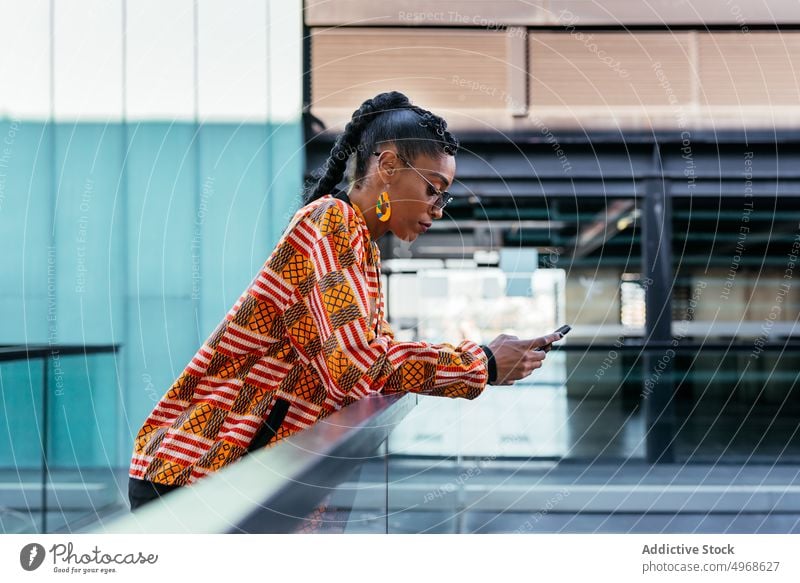 Trendige Frau benutzt Smartphone auf Terrasse benutzend Stil soziale Netzwerke fettarm Zaun Gebäude modern jung ethnisch Balkon Browsen trendy Glas Telefon