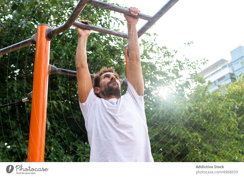 Spanischer Sportler beim Training am Barren Sportpark Park Übung Fitness Ausdauer stark hängen Fokus männlich Erwachsener hispanisch konzentriert ethnisch Baum