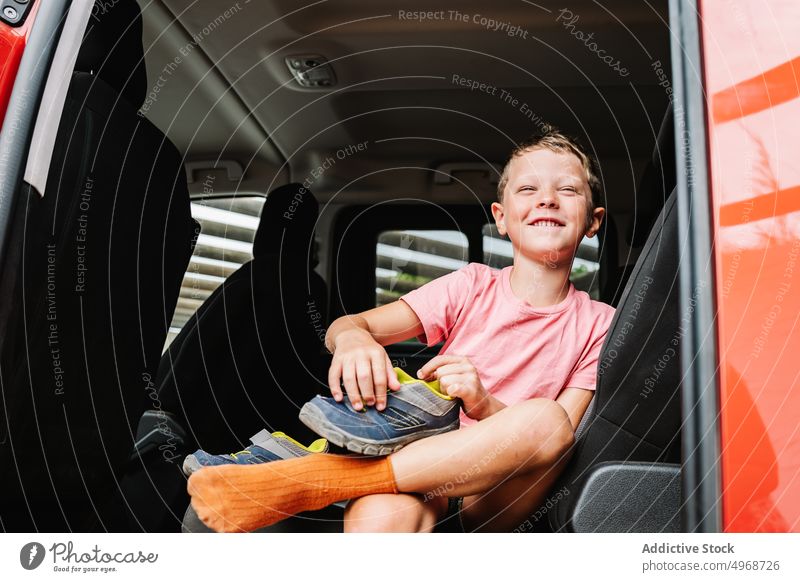Lächelnder Junge, der sich auf dem Rücksitz einen Schuh anzieht angezogen PKW befestigen Autoreise heiter Wochenende froh vorbereiten Glück Passagier Kind