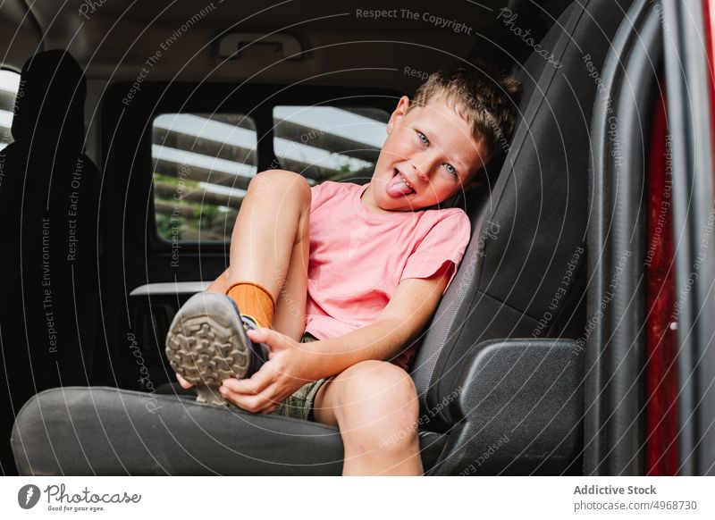 Lächelnder Junge, der sich auf dem Rücksitz einen Schuh anzieht angezogen PKW befestigen Autoreise heiter Wochenende froh vorbereiten Glück Passagier Kind