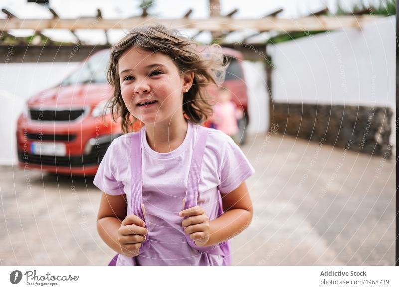 Mädchen mit Rucksack in der Nähe des Autos im Hof Lächeln Wochenende Sommer PKW reisen bereit Glück Kind Hinterhof lässig tagsüber Fahrzeug froh sorgenfrei