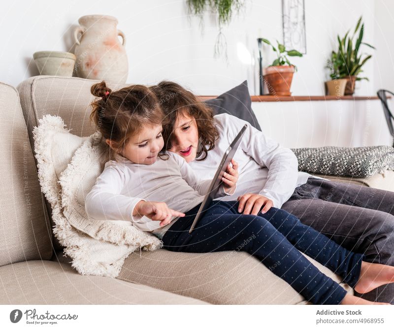Kinder benutzen Tablet auf dem Sofa Mädchen Tablette Gerät Appartement Zusammensein Schwester Kindheit heimwärts benutzend Komfort Apparatur bezaubernd Lügen