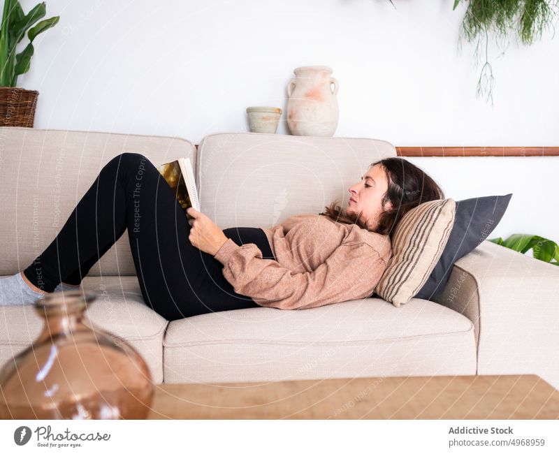 Frau auf Sofa liegend mit Buch Liege Hobby Wohnzimmer modern Appartement Konzentration ernst lesen Freizeit Fokus heimwärts Literatur Wissen Zeitvertreib