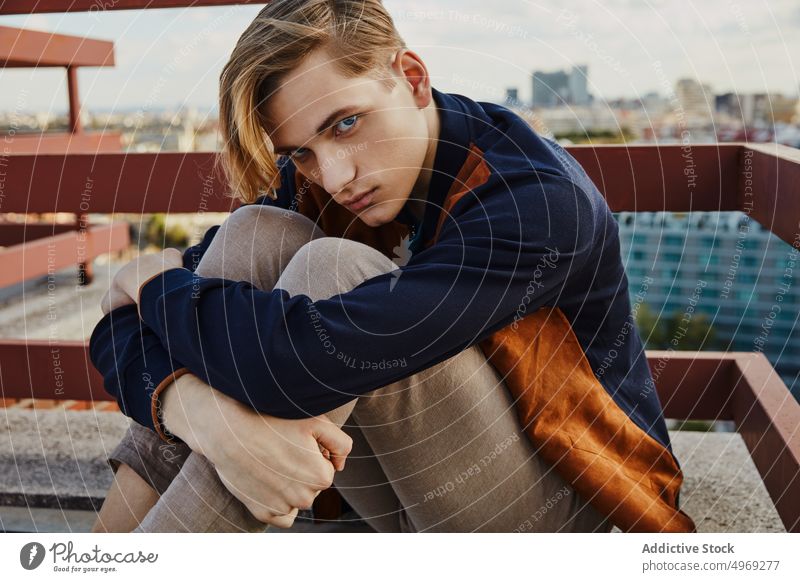Junger blonder Mann sitzt auf dem Dach eines Gebäudes Sitzen gutaussehend entspannt urban trendy stylisch Model jung Glamour männlich cool Eleganz Typ