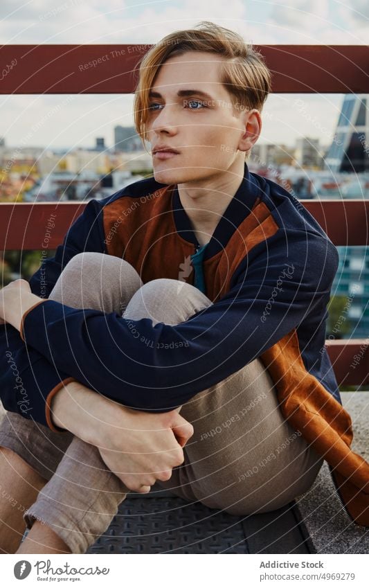 Junger blonder Mann sitzt auf dem Dach eines Gebäudes Sitzen gutaussehend entspannt urban trendy stylisch Model jung Glamour männlich cool Eleganz Typ