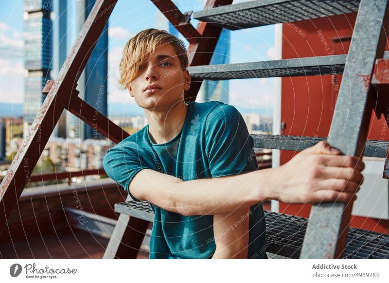 Modischer junger Mann sitzt auf einer Leiter auf dem Dach Sitzen Laufmasche gutaussehend entspannt urban trendy stylisch Model cool männlich Typ attraktiv Glück