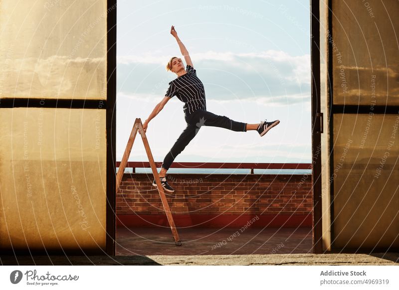 Junge Choreografin posiert auf einer Trittleiter auf dem Dach Athlet posierend Ausgeglichenheit strecken beweglich talentiert zierlich leer jung Mann männlich