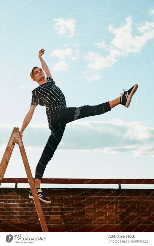 Junge Choreografin posiert auf einer Trittleiter auf dem Dach Athlet posierend Ausgeglichenheit strecken beweglich talentiert zierlich leer jung Mann männlich