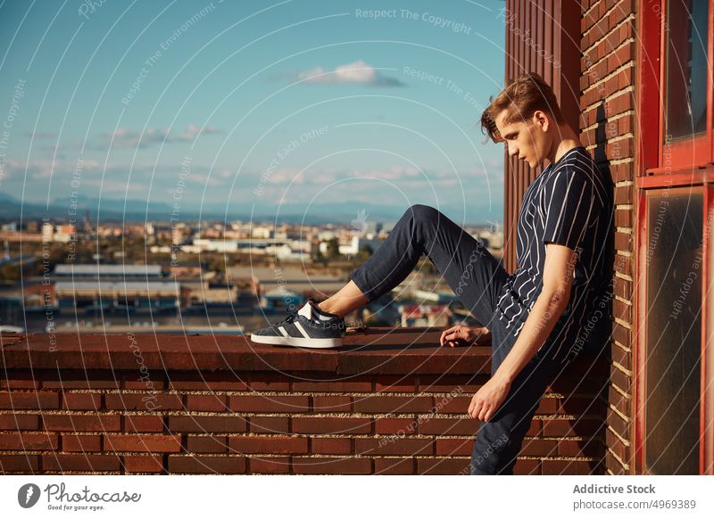 Hübscher junger Mann auf dem Dach sitzend Sitzen Gebäude Straße gutaussehend entspannt urban trendy stylisch Model Sommer männlich blond attraktiv Glück ernst