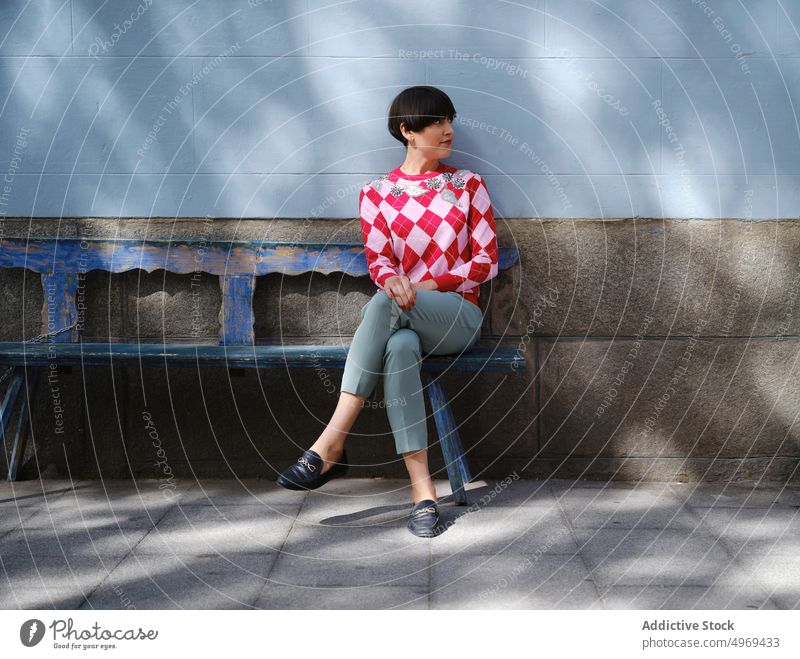 Frau in trendigem Outfit entspannt auf einer Bank in der Stadt Großstadt stilvoll sich[Akk] entspannen Stil Frisur bob schäbig hölzern Windstille Straße ruhen