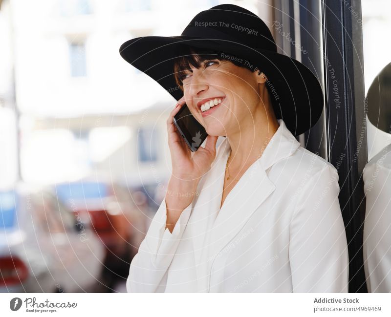 Elegante Frau mit Hut spricht in der Stadt mit ihrem Smartphone charmant elegant sprechen Straße reden Stil benutzend trendy Damenschuhe Gebäude Mobile Telefon