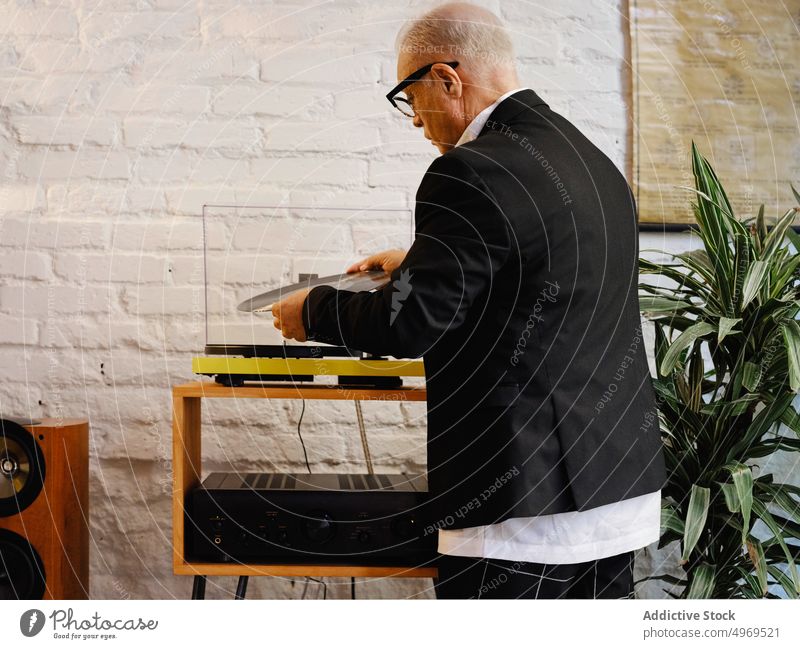 Älterer Mann legt Schallplatte in Plattenspieler Aufzeichnen Spieler Vinyl Musik gealtert Scheibe Nostalgie Senior zuhören retro elegant männlich Hobby genießen