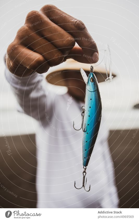 Unbekannter Angler mit Stecker in der Hand Fischer blau Fischen anpacken ködern Küste Ufer Vorrat Hobby Gerät vorbereiten männlich Meeresufer Seeküste Hut