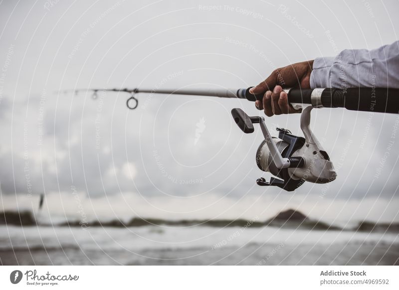 Unbekannter Fischer beim Fischen am Ufer Stab Spinnrolle Küste Vorrat Hobby fangen Fähigkeit männlich Meeresufer Seeküste Angler Lifestyle ruhen Freizeit Typ