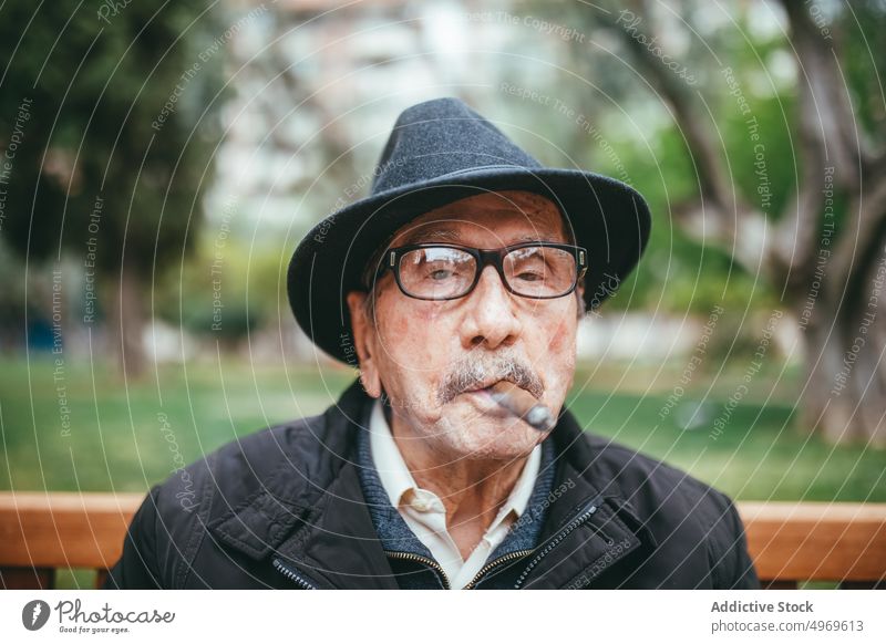Älterer Mann raucht Zigarre auf der Straße Senior älter gealtert Rauch Park Habitus Nikotin Bank Hut lässig Lifestyle Großstadt Schnurrbart besinnlich