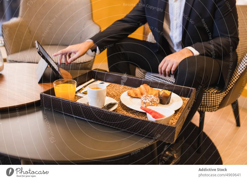 Unbekannter Mann mit Tablet am Tisch mit Tablett mit Essen Unternehmer Tablette online Dessert Kaffee Hotel Browsen Lebensmittel dienen männlich Gerät Morgen