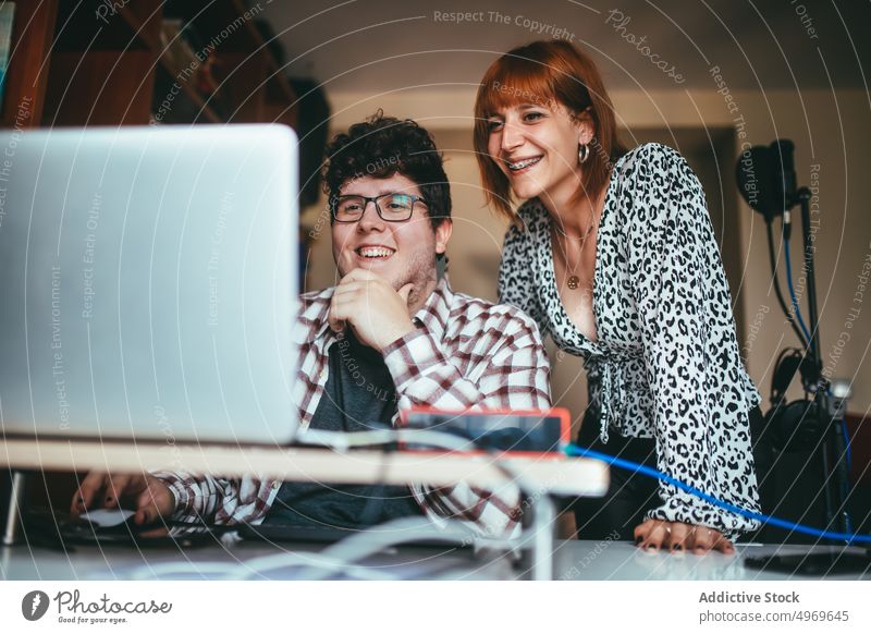 Lächelnde Sängerin und Produzentin teilen sich zu Hause einen Laptop interagieren heiter Kinn berühren Arbeit heimwärts benutzend Apparatur Mann Frau Gerät