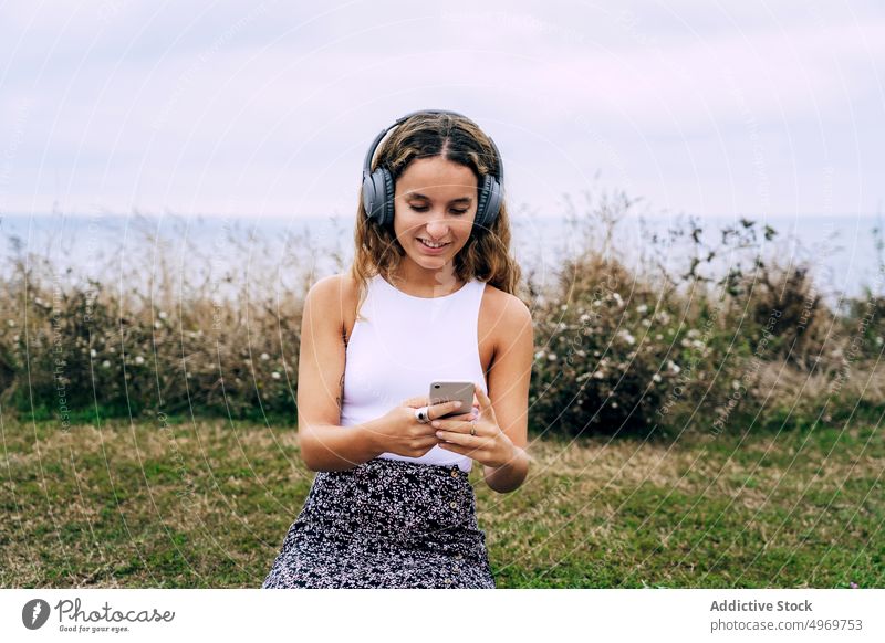 Frau mit Kopfhörern sitzt mit Smartphone an einer gemauerten Wand Musik benutzend Apparatur Gerät hören Mobile Telefon jung Glück klug attraktiv Anschluss