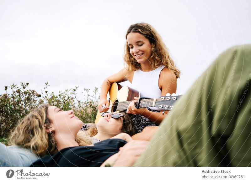 Frau lächelt und spielt Gitarre für Freunde auf einem Feld Spielen genießend hören jung spielen romantisch Instrument Freundschaft heiter Partnerschaft
