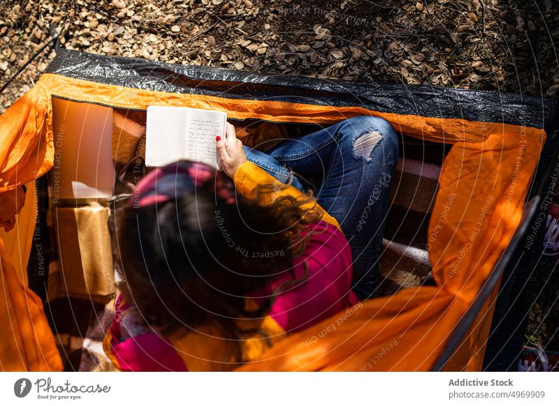 Anonyme Frau sitzt im Zelt und schreibt Notizen in ein Notizbuch Lager genießen Gras im Freien sich[Akk] entspannen Wald Feiertage Abenteuer Feld Landschaft