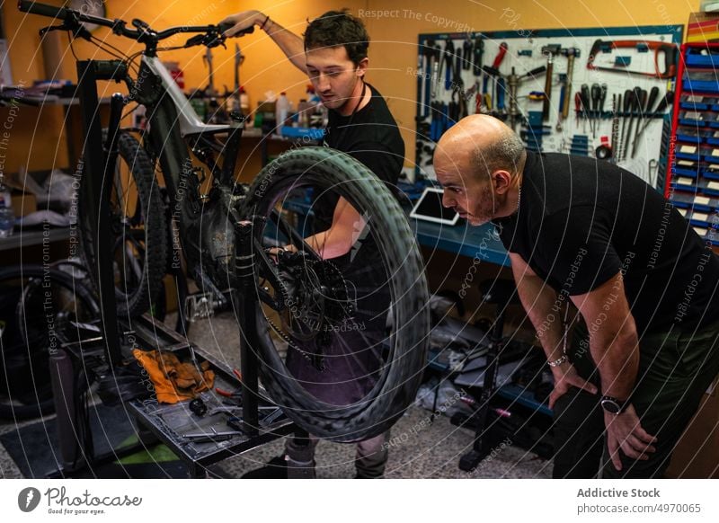 Männliche Mechaniker untersuchen ein Fahrrad in der Werkstatt Reparatur Arbeit Männer Zusammensein Dienst Erwachsener Laden Job professionell prüfen fixieren