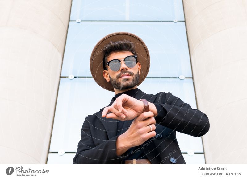 Maskuliner Mann mit trendiger Sonnenbrille hinter einem Geländer in der Stadt Mode Stil Individualität kreativ Design Zeitgenosse maskulin Hut Jacke Macho