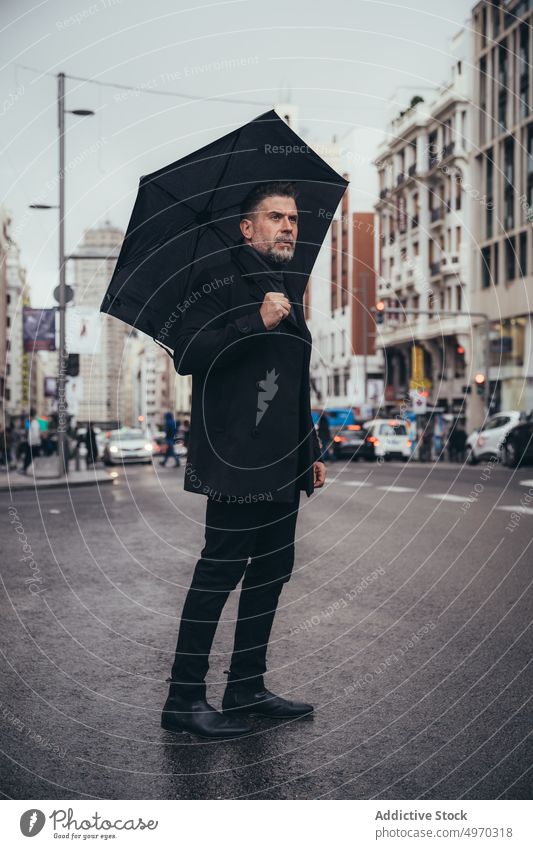 Nachdenklicher Geschäftsmann mittleren Alters mit Regenschirm auf der Straße Unternehmer stilvoll Spaziergang Straßenbelag regnerisch trendy Großstadt elegant