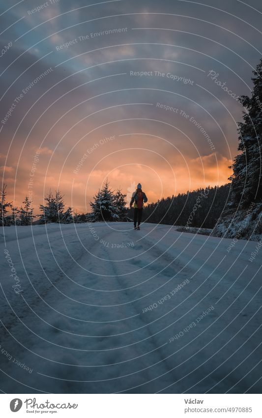 Unverfälschtes Porträt eines Mannes in Winterkleidung, der am Ende eines Weges steht und den Sonnenaufgang in der verschneiten Gegend der Stare Hamry Beskiden beobachtet, Tschechische Republik