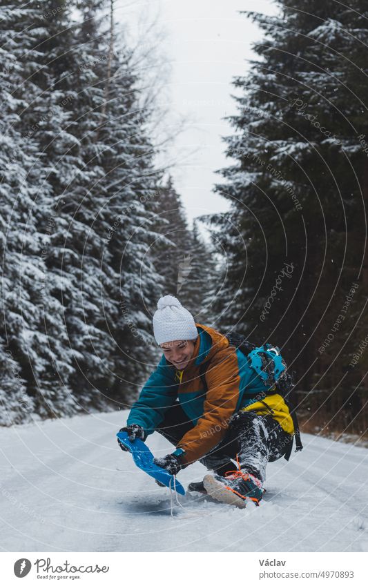 Unverfälschtes Porträt eines jungen Mannes, der während der Wintersaison in einem verschneiten Gebiet eine farbenfrohe Winterwanderjacke, warme Kleidung und eine weiße Mütze trägt. Reiten ein Plastik-Snowboard